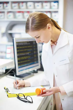 woman pharmacist holding a bottle of pills and writing on a clipboard