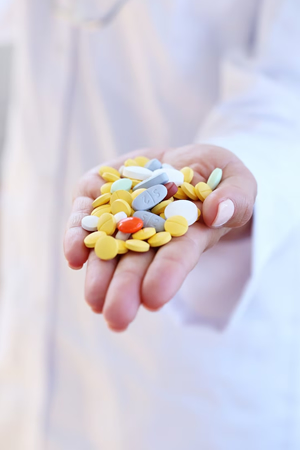 yellow, white, blue, and orange pills in a white person's hand